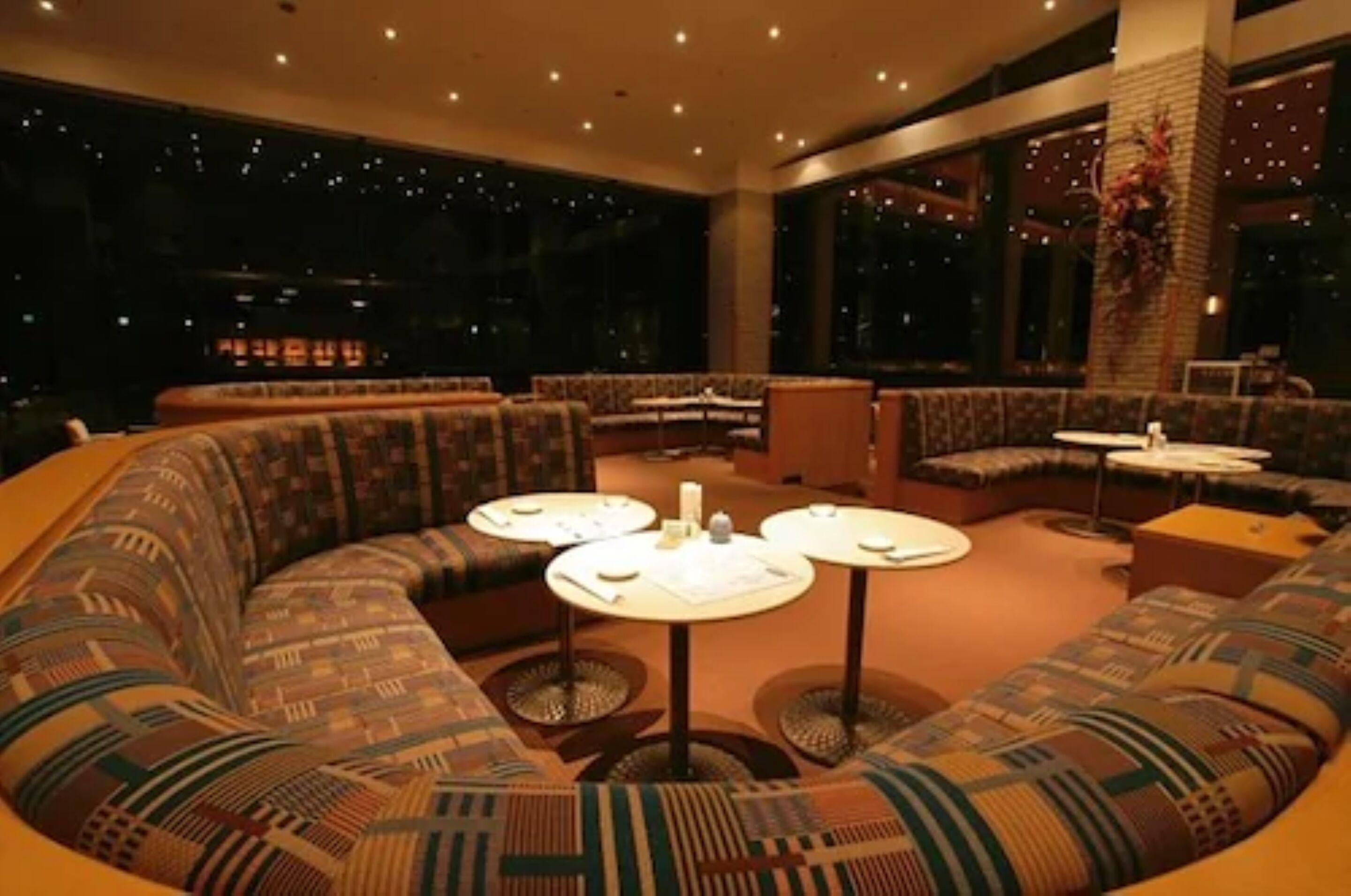 A modern lounge with a curved sofa, round tables, and large windows offering a night view.