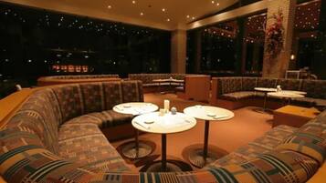 A modern lounge with a curved sofa, round tables, and large windows offering a night view.