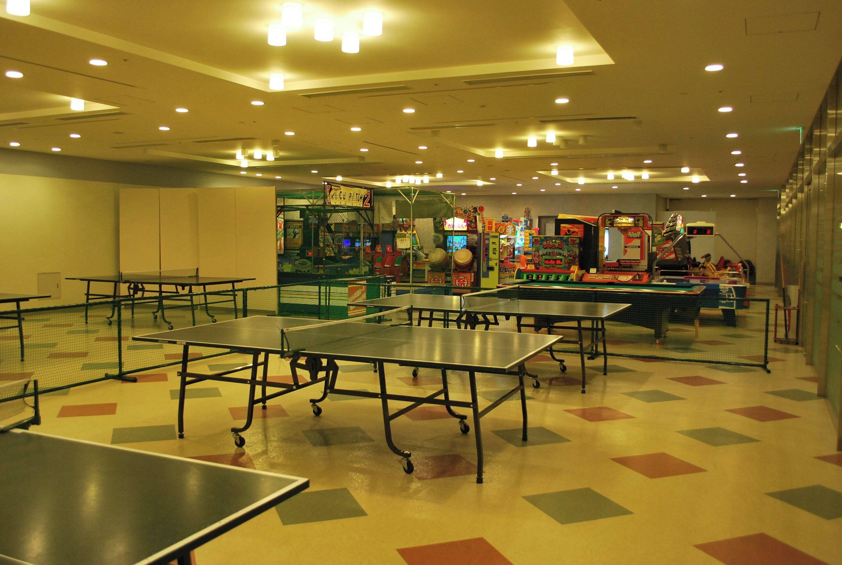 Una habitación con mesas de ping pong, juegos de arcade y un estampado de suelo colorido.