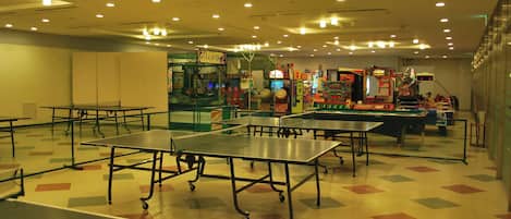 Una habitación con mesas de ping pong, juegos de arcade y un estampado de suelo colorido.