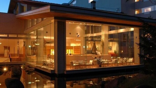 A modern hotel with a glass facade, a pool area, and a dining space visible through the windows. - Kussharo Prince Hotel (Teshikaga)