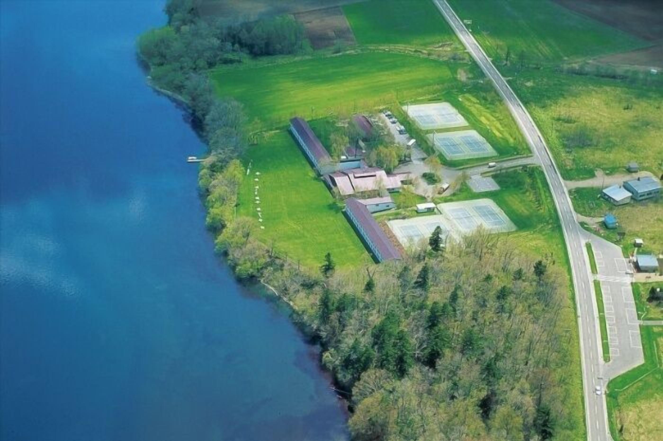 An aerial view of a coastal property with a road, green fields, and buildings with solar panels.
