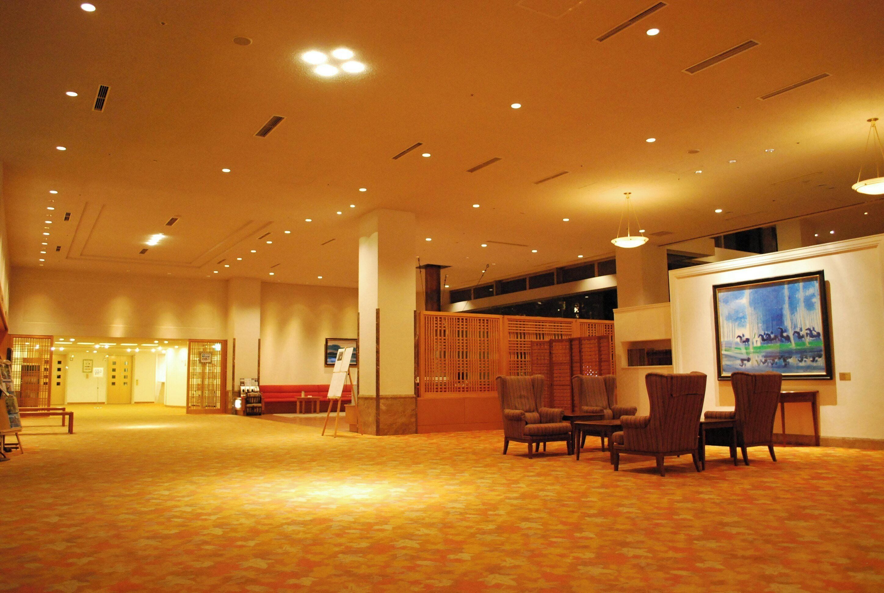 A spacious lobby with a carpeted floor, seating area with chairs, a reception desk, and a large framed artwork on the wall.