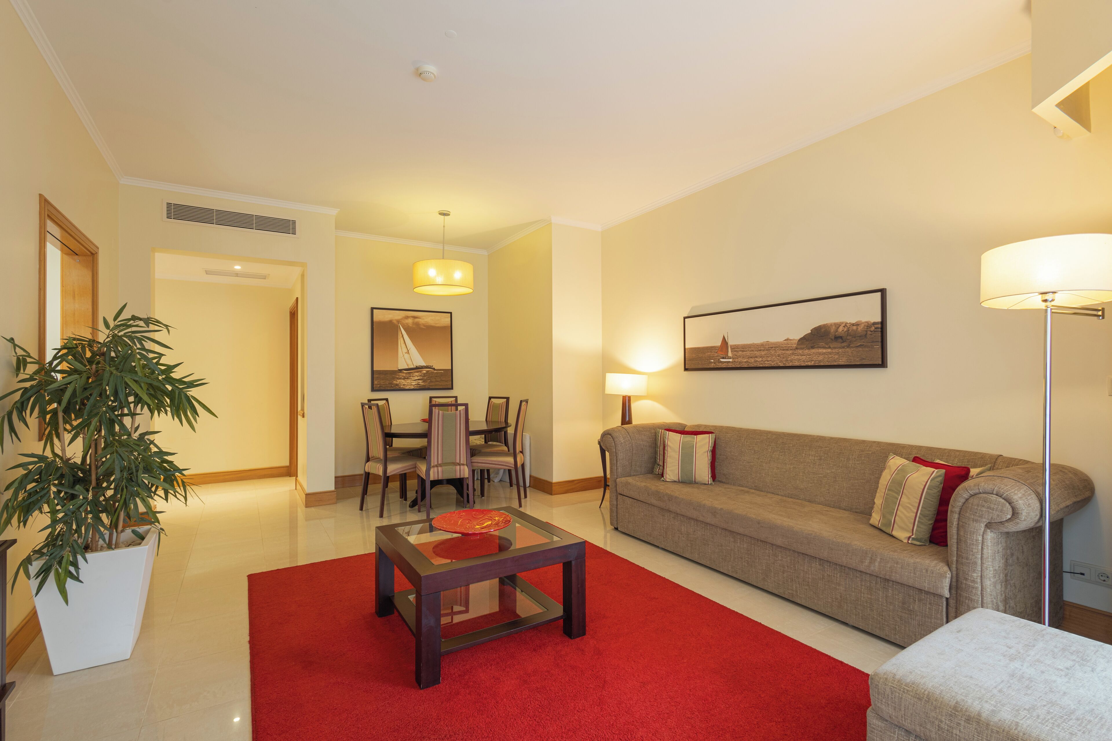 A living room with a red carpet, a sofa, a coffee table, and a dining area with chairs and a table.