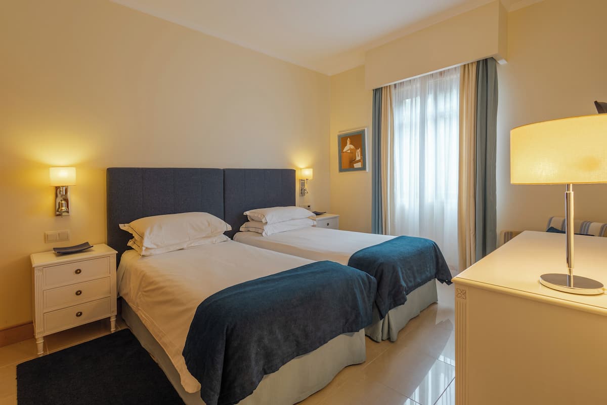 Ein Hotelzimmer mit zwei Betten, einem Schreibtisch, einem Stuhl, einem Nachttisch und einer Lampe.