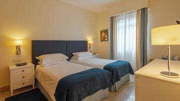 Une chambre d’hôtel avec deux lits, un bureau, une chaise, une table de chevet et une lampe.