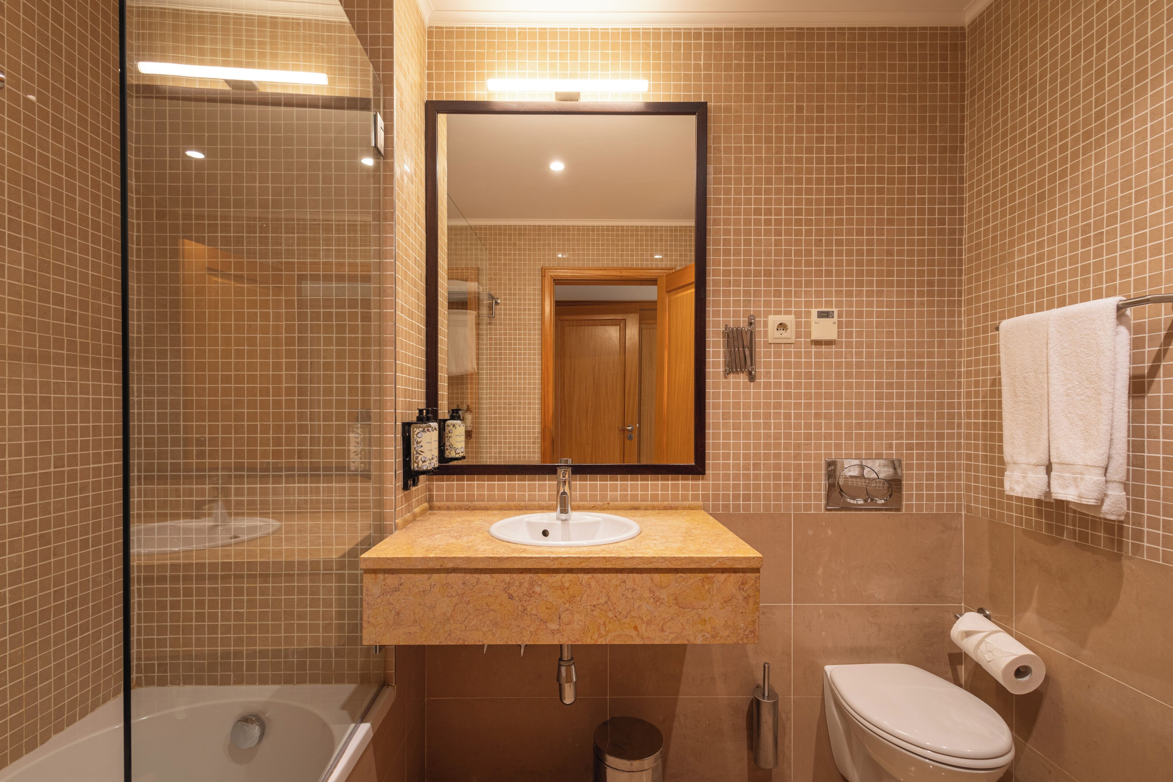 A bathroom with a glass-enclosed shower, a sink with a mirror above it, and a toilet.