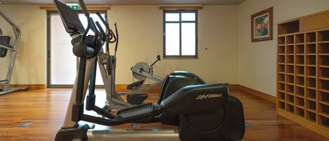 Un gimnasio con equipo de cardio, suelo de madera, una ventana y un cuadro en la pared.