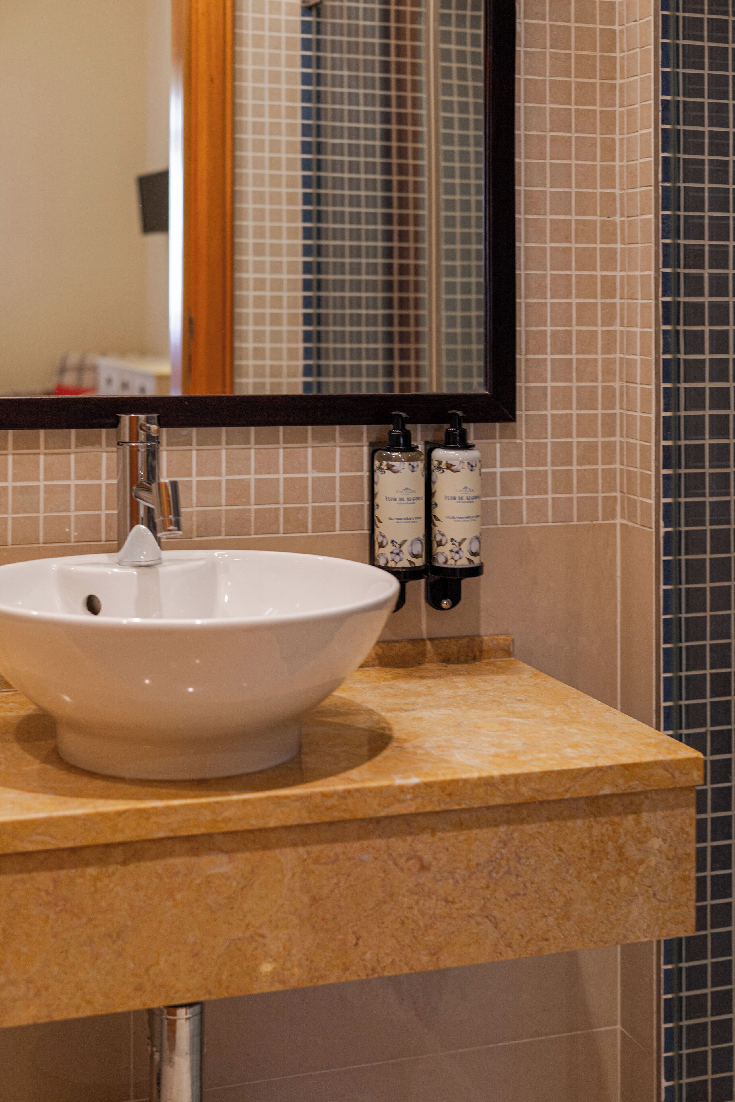 A bathroom sink with a mirror above it, a towel rack with bottles, and tiled walls.