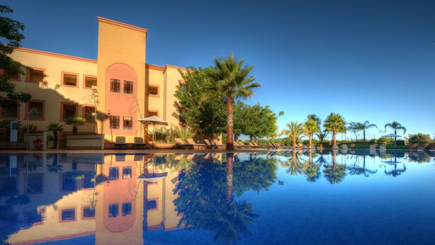 A hotel with a swimming pool reflecting the building and palm trees. - The Residences Vilamoura (Loulé)