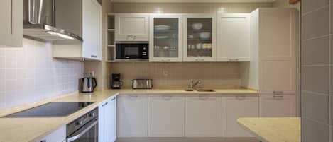 A modern kitchen with white cabinets, a stainless steel range hood, a built-in oven, and a countertop with a coffee maker and toaster.