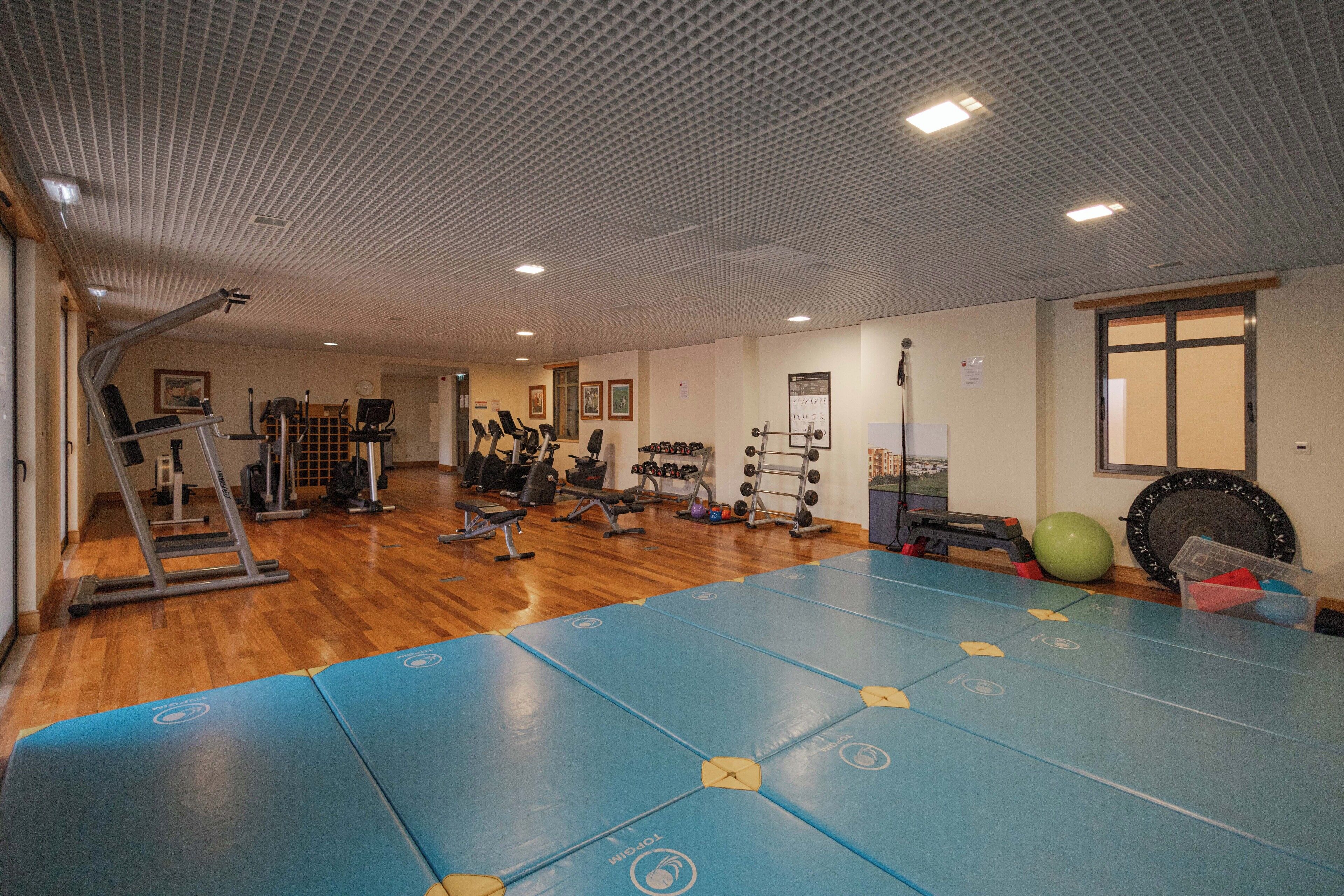 Een sportschool met trainingsapparatuur, matten en een houten vloer.