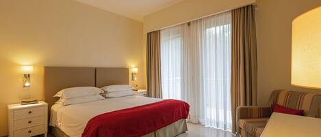 A hotel room with a large bed, a bedside table, a chair, and a window with curtains.