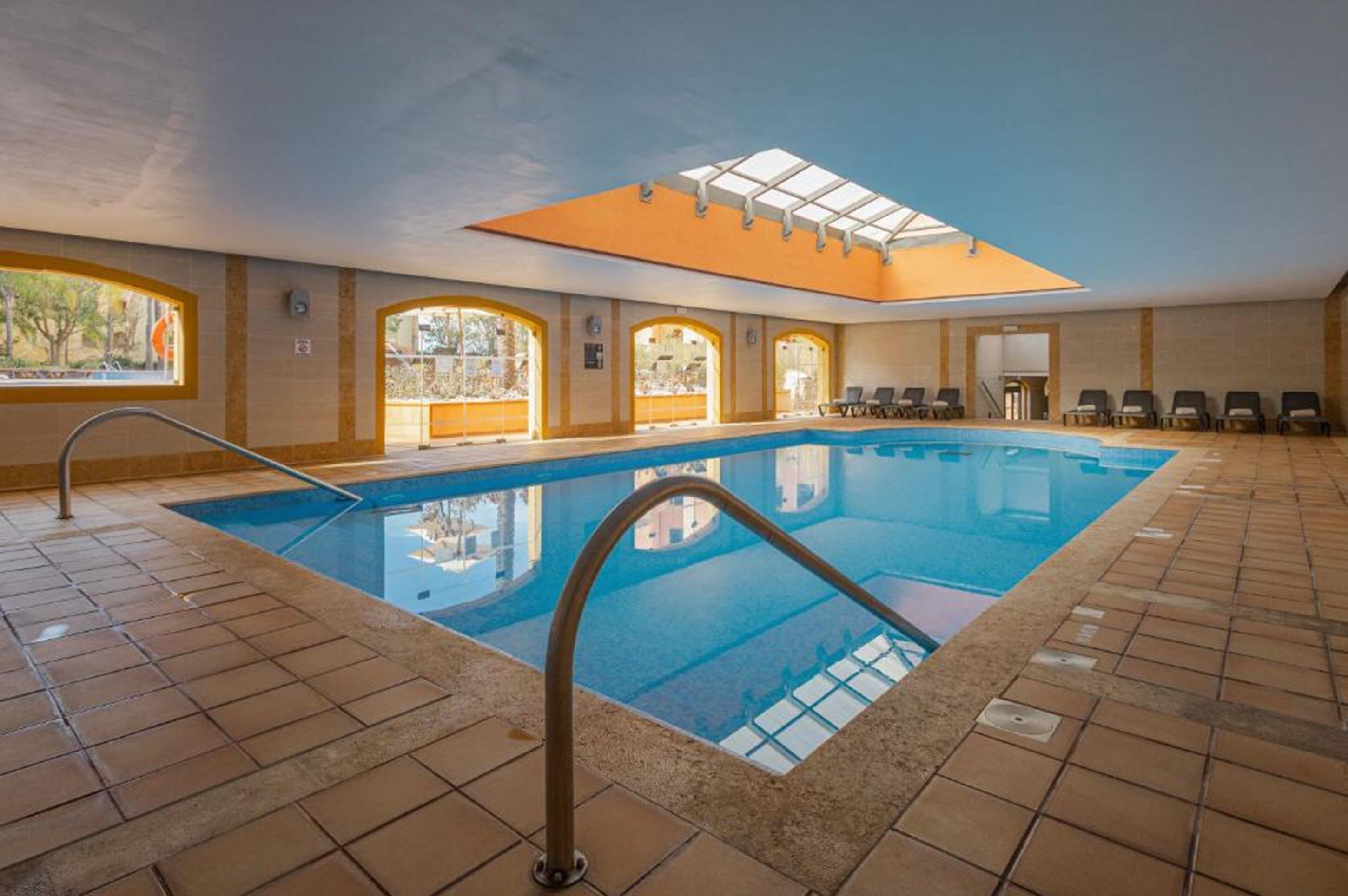 An indoor swimming pool with clear glass walls, a tiled floor, and a skylight above.