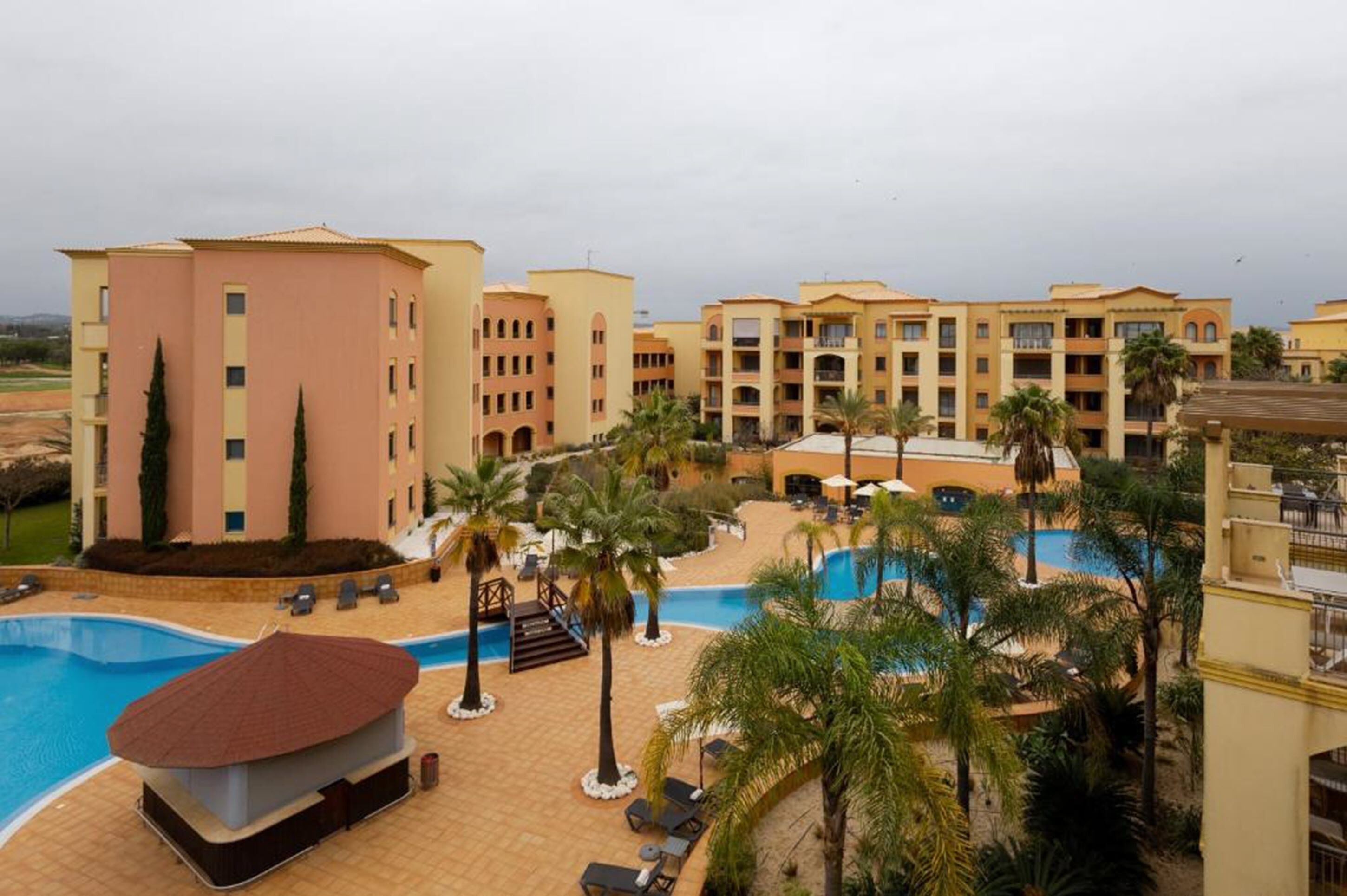A hotel with a swimming pool, palm trees, and a view of the surrounding landscape.