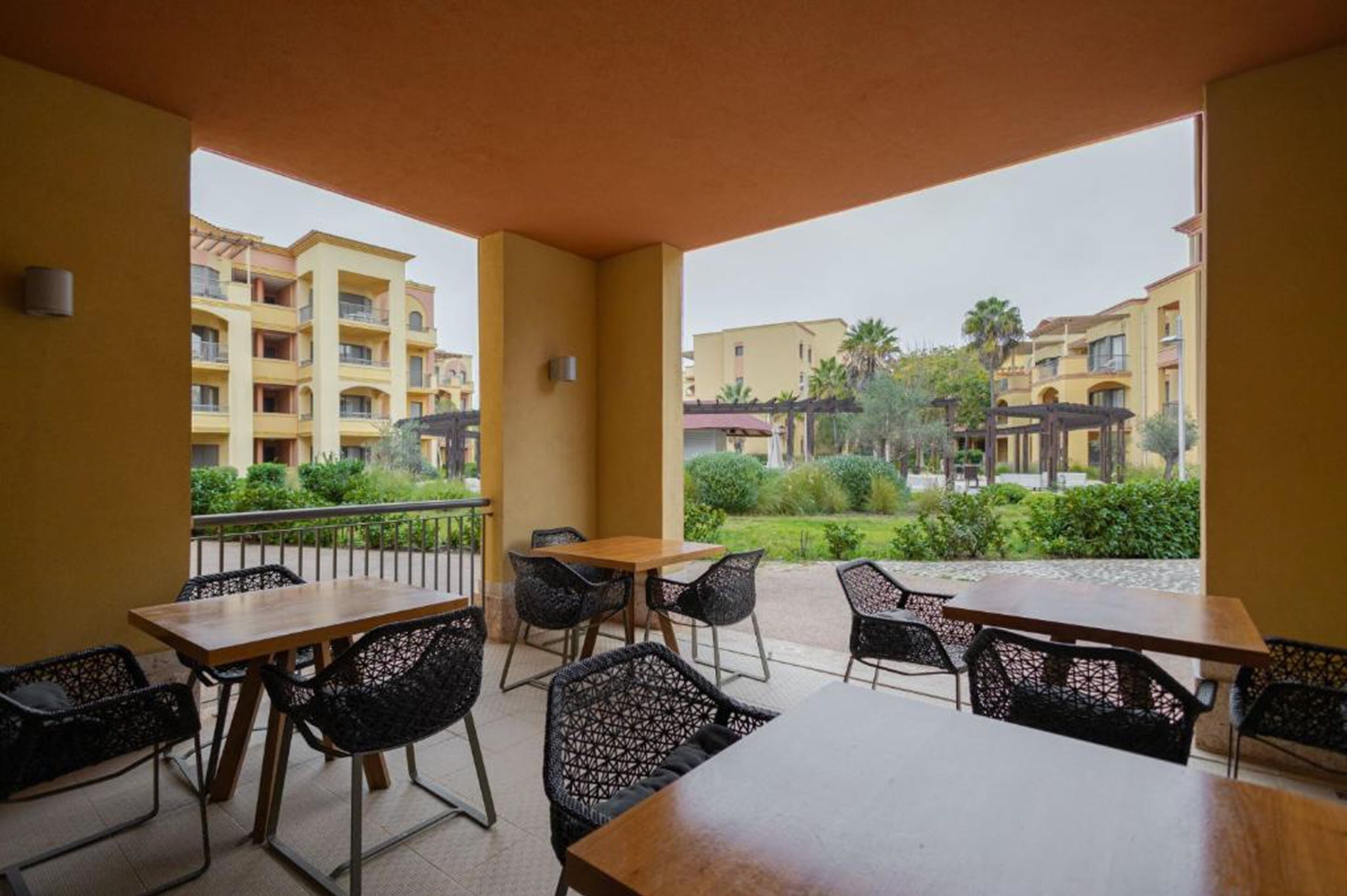 Un balcón con mobiliario exterior, vista a un edificio residencial y cielo despejado.