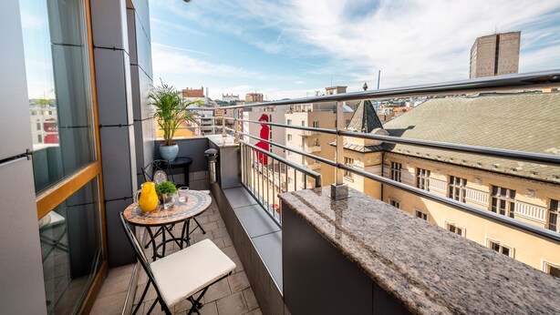 A balcony with a table, chairs, a potted plant, and a view of the cityscape. - Hotel Danubia Gate (Bratislava)