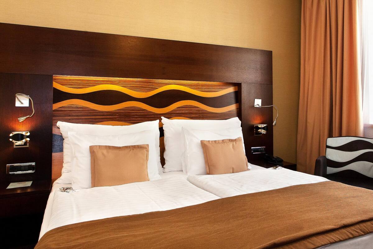 A hotel room with a large bed, two bedside tables, a chair, and a window with curtains.