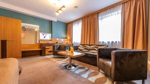 A hotel room with a sofa, a small table with a vase, a TV, and a kitchen area. - Hotel Danubia Gate (Bratislava)
