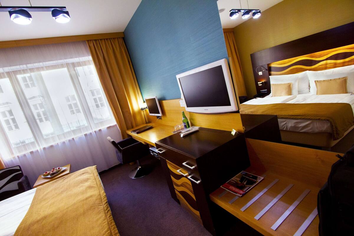A hotel room with a desk, a bed, a television, and a window with curtains.