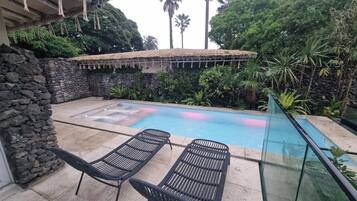 A pool area with stone walls, two lounge chairs, and tropical vegetation.