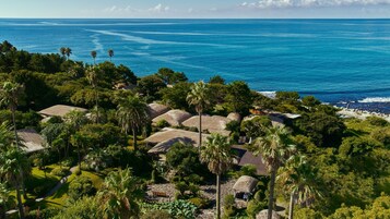 A coastal resort with thatched-roof huts, lush greenery, and a view of the ocean.