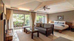 A modern hotel room with a sofa, a glass coffee table, a bed with a nightstand, and a ceiling fan. - Seaes Hotel & Resort (Seogwipo)