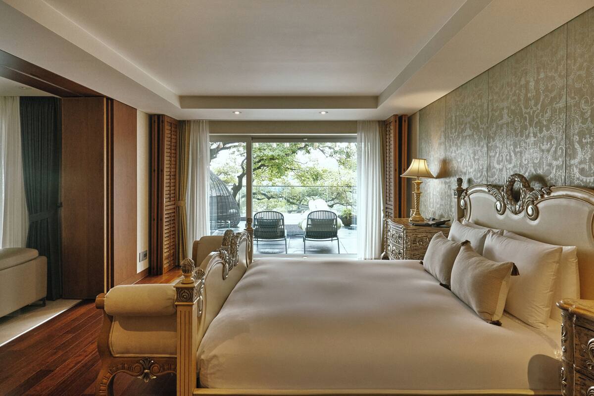 Une chambre spacieuse avec un grand lit, un coin salon avec un fauteuil et une vue sur l’extérieur grâce à une porte vitrée.