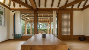 Une pièce avec une table en bois, de grandes fenêtres, un tatami et un paravent en papier.