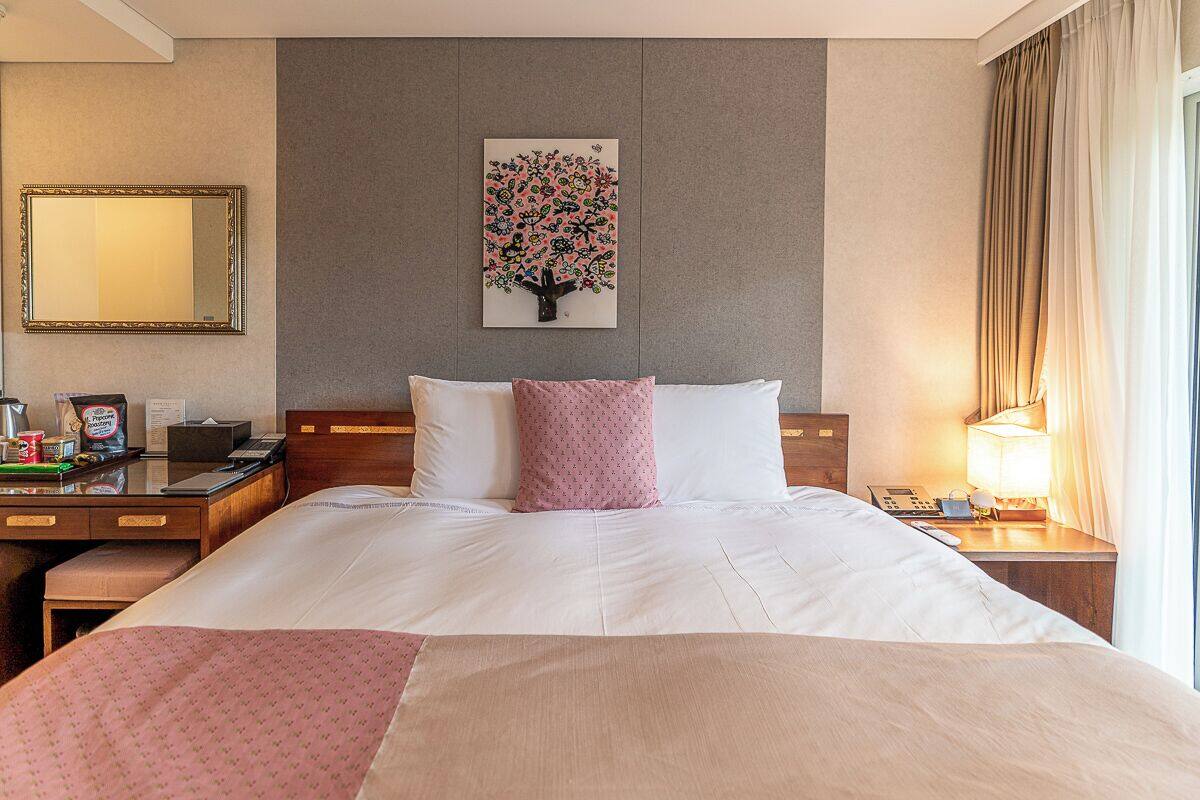 Une chambre d’hôtel avec un grand lit, un bureau avec un téléphone, un miroir et une œuvre d’art accrochée au mur.