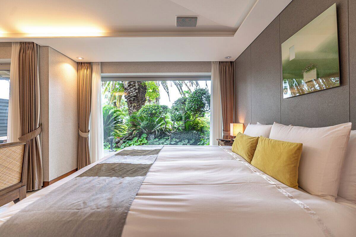 Une chambre d’hôtel avec un grand lit, une vue sur la verdure et un tableau accroché au mur.