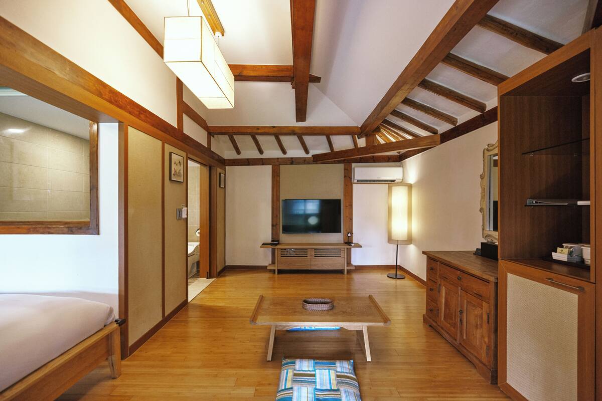 Une chambre avec un lit, une télévision, une armoire en bois et une table avec un coussin.