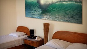 Camera d'albergo con due letti, un comodino, un quadro raffigurante un'onda e un vaso con piante essiccate.