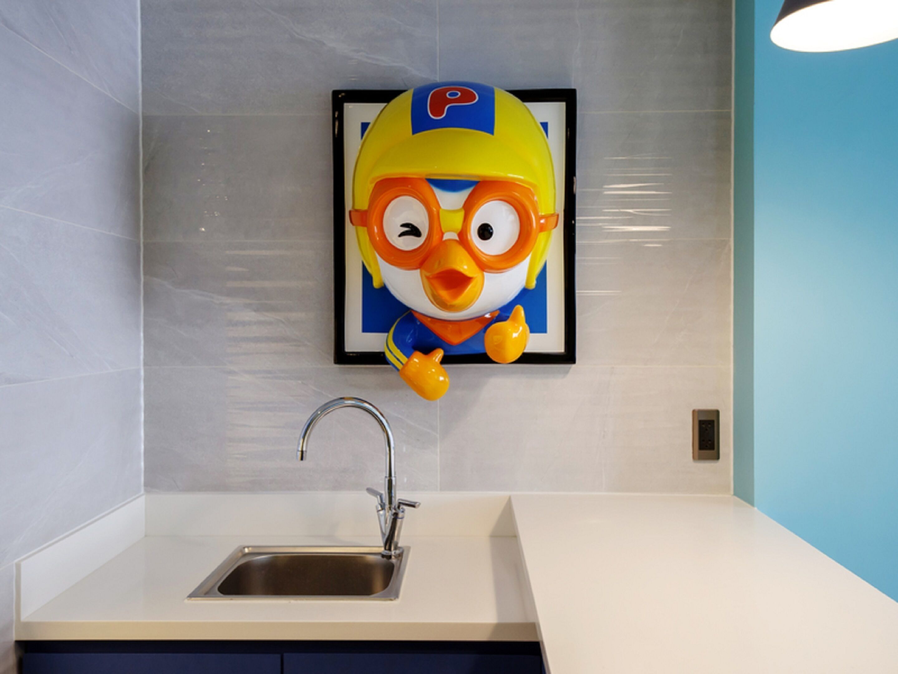 Uma cozinha com uma pia, um quadro com um personagem de desenho animado e uma parede azul.