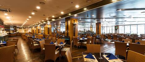A spacious restaurant with multiple dining tables and chairs, large windows, and a high ceiling with recessed lighting.