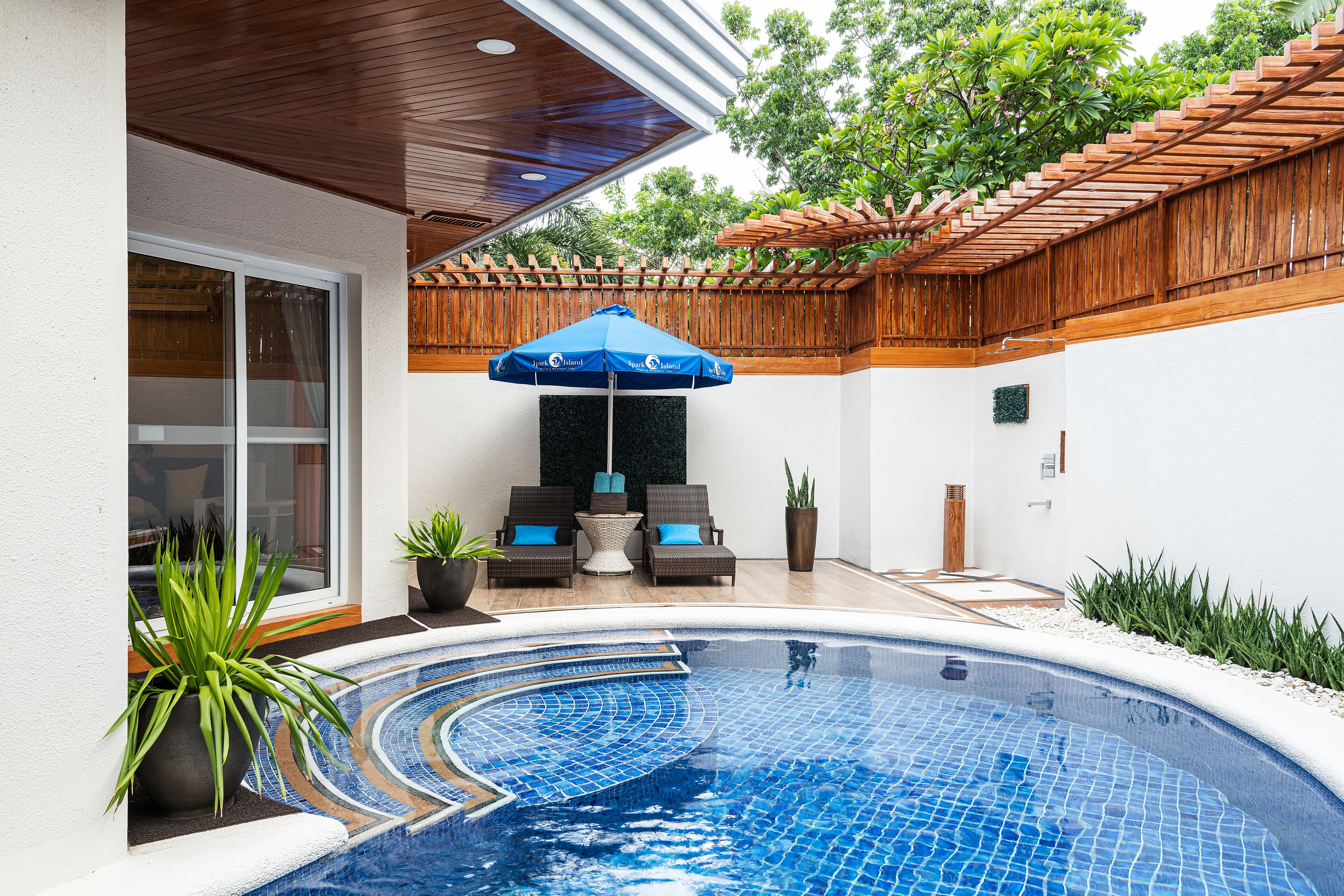 A swimming pool with a blue mosaic tile design, surrounded by a wooden pergola and potted plants.