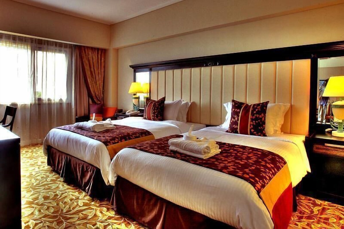 Habitación de hotel con dos camas, un ventanal con cortinas, un escritorio y una silla.