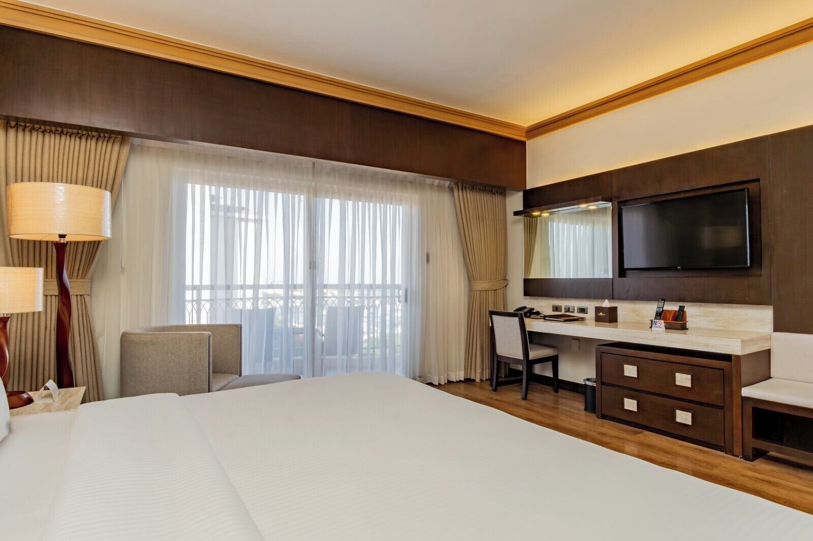 A hotel room with a large bed, a desk, a chair, a TV, and a minibar.