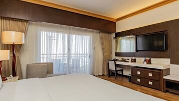A hotel room with a large bed, a desk, a chair, a TV, and a minibar.