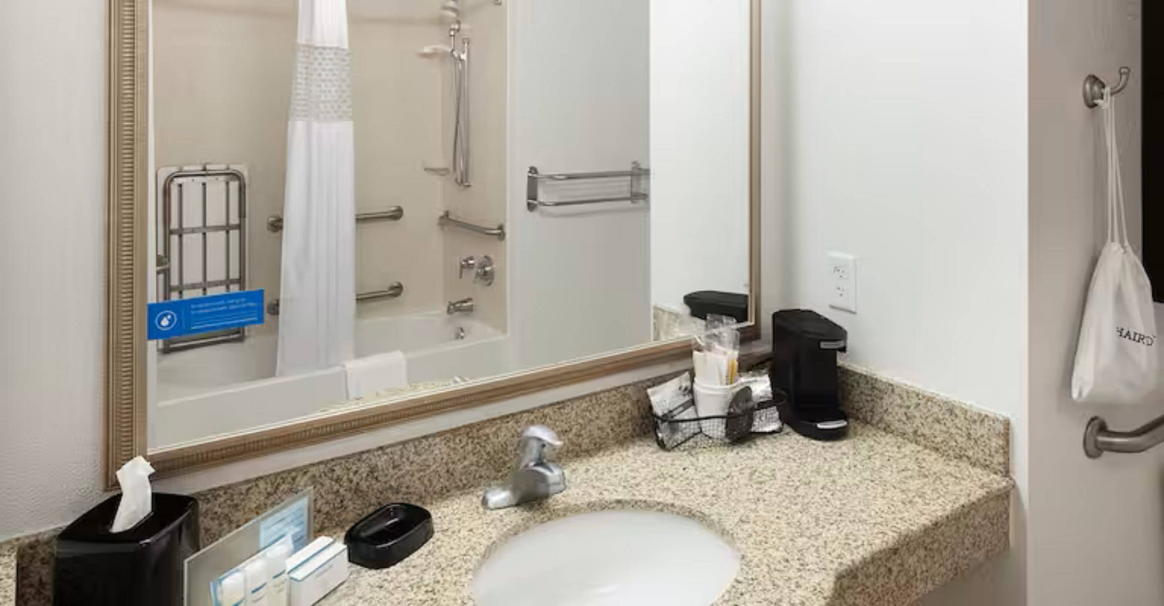 Een hotelbadkamer met een wastafel, spiegel, handdoekhouder en een douche.