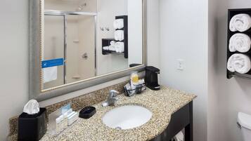 Un baño de hotel con lavamanos de encimera de granito, un espejo, un perchero y un dispensador de jabón.