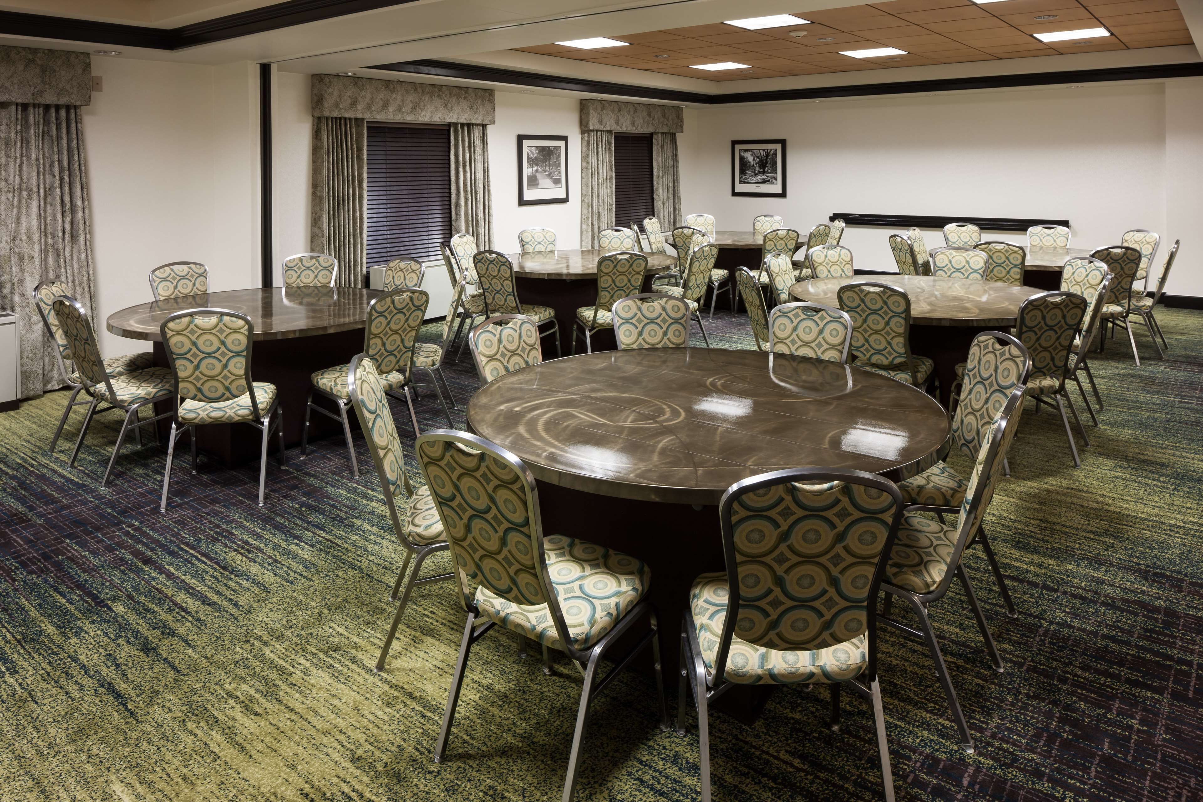 A conference room with a large round table surrounded by patterned chairs, carpeted flooring, and framed pictures on the walls.