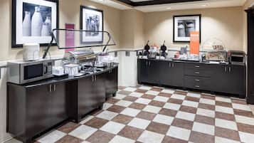 A hotel kitchen with a checkered floor, a buffet counter with various food items, and framed pictures on the walls.