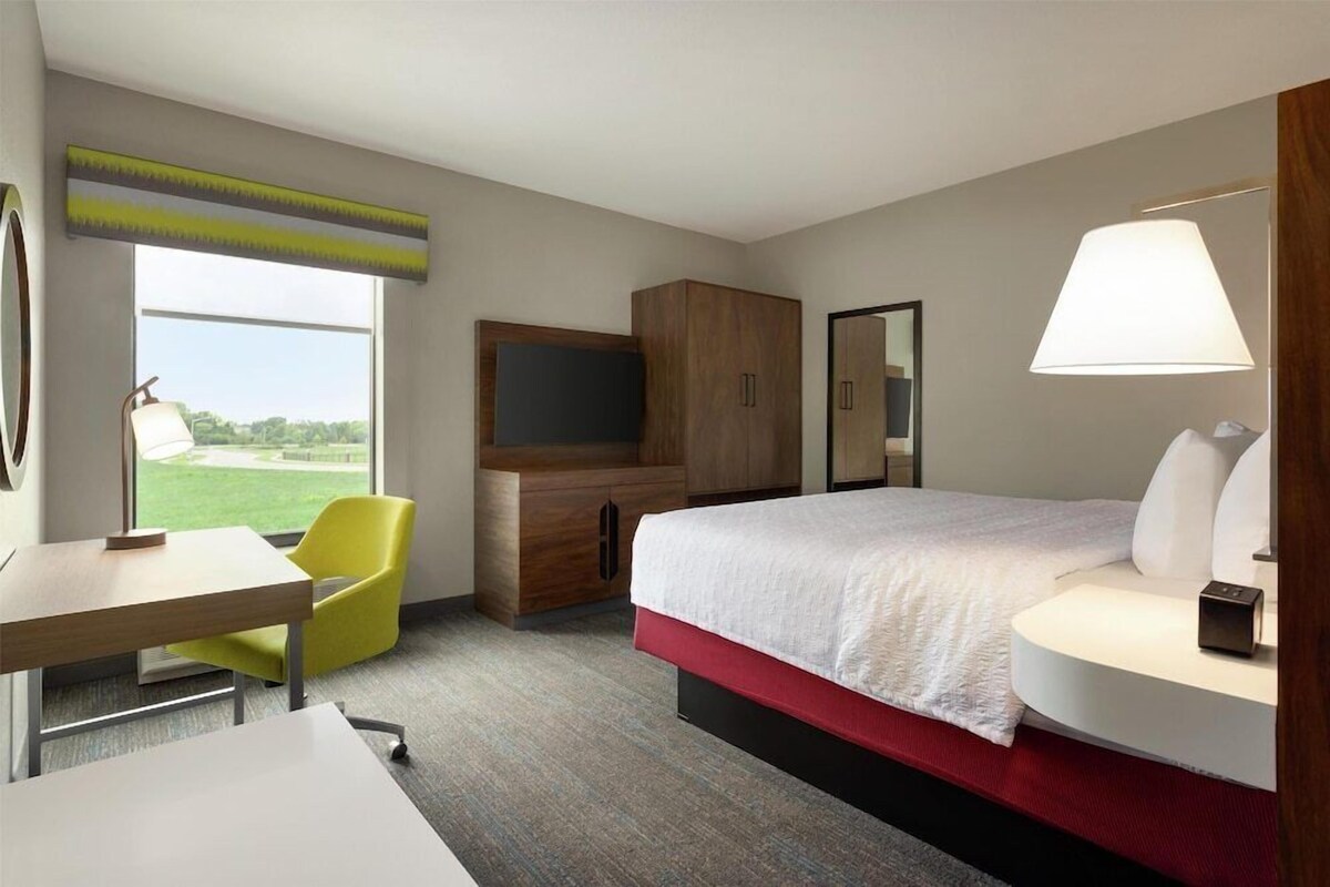 A hotel room with a bed, a desk, a chair, a TV, and a window with a view.