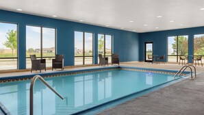 A swimming pool with clear blue water, surrounded by large windows offering views of the outdoors.