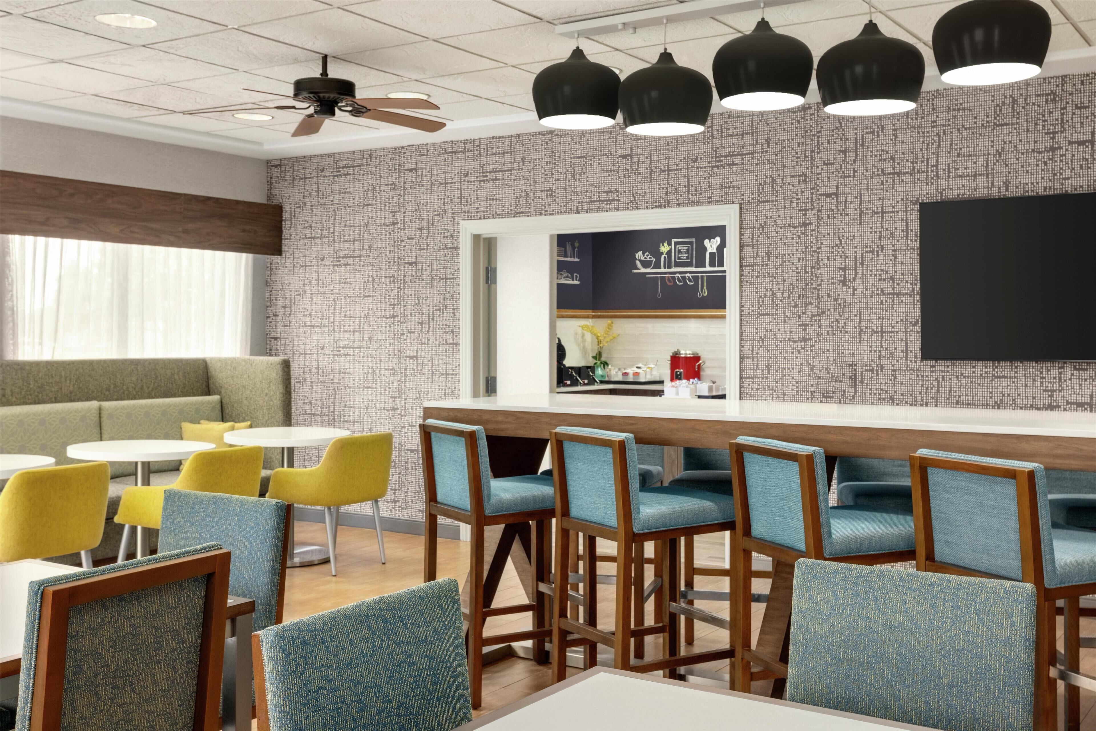 A modern bar area with high stools, a counter, and a seating area with yellow chairs.
