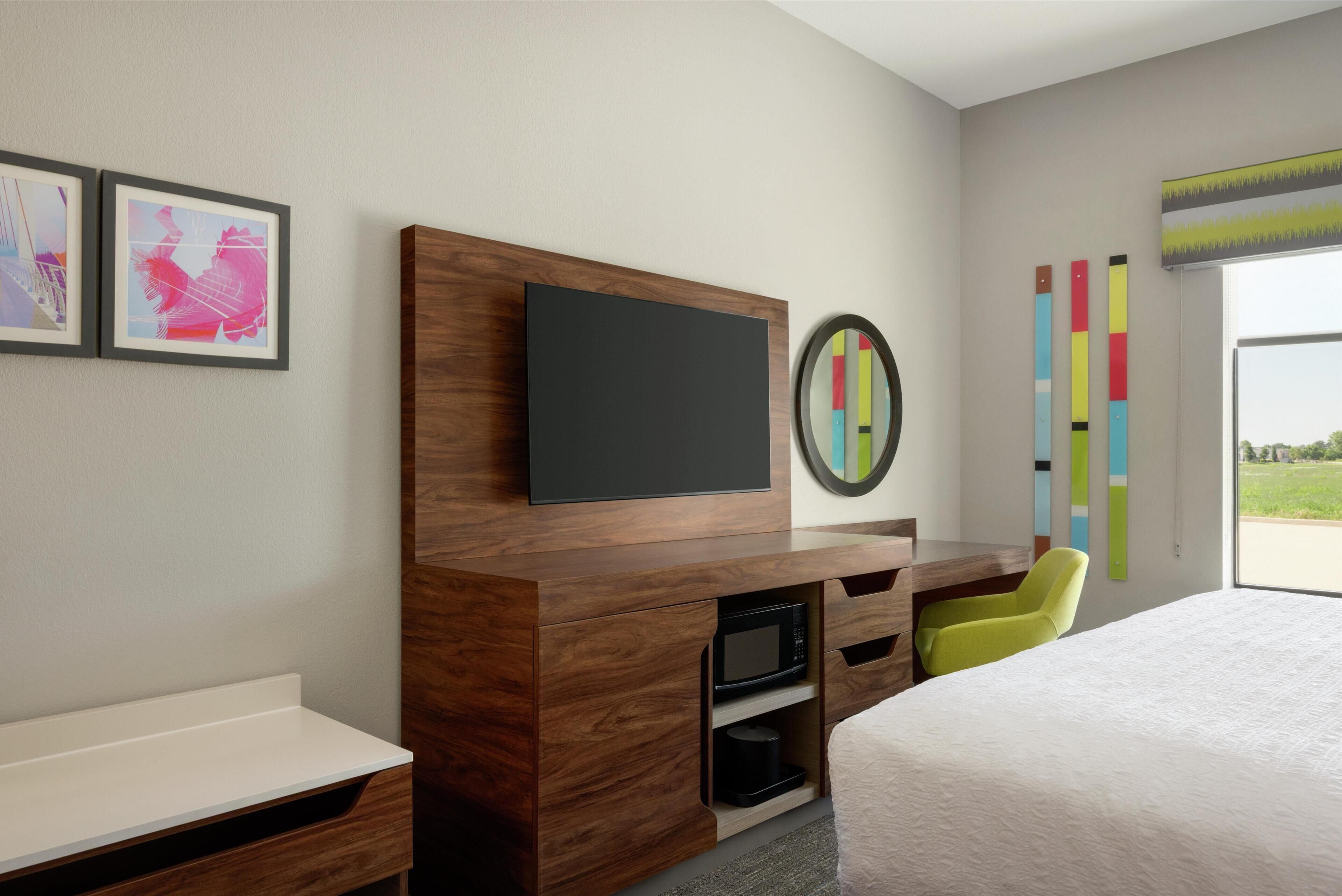 Une chambre d’hôtel moderne dotée d’un bureau en bois, d’un téléviseur à écran plat, d’un four à micro-ondes, d’un lit et offrant une vue sur l’extérieur.