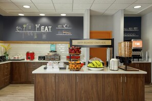 Una barra de desayuno con un letrero que dice "HAPPY BREAKFAST STARTS HERE" y diversas opciones de comida como frutas y pasteles.