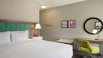 A hotel room with a large bed, a desk with a chair, a lamp, and two framed pictures on the wall.