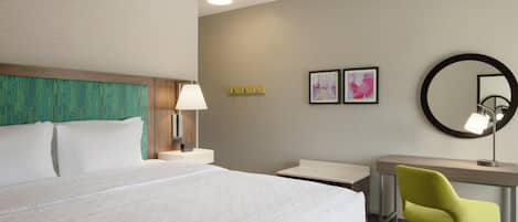 A hotel room with a large bed, a desk with a chair, a lamp, and two framed pictures on the wall.